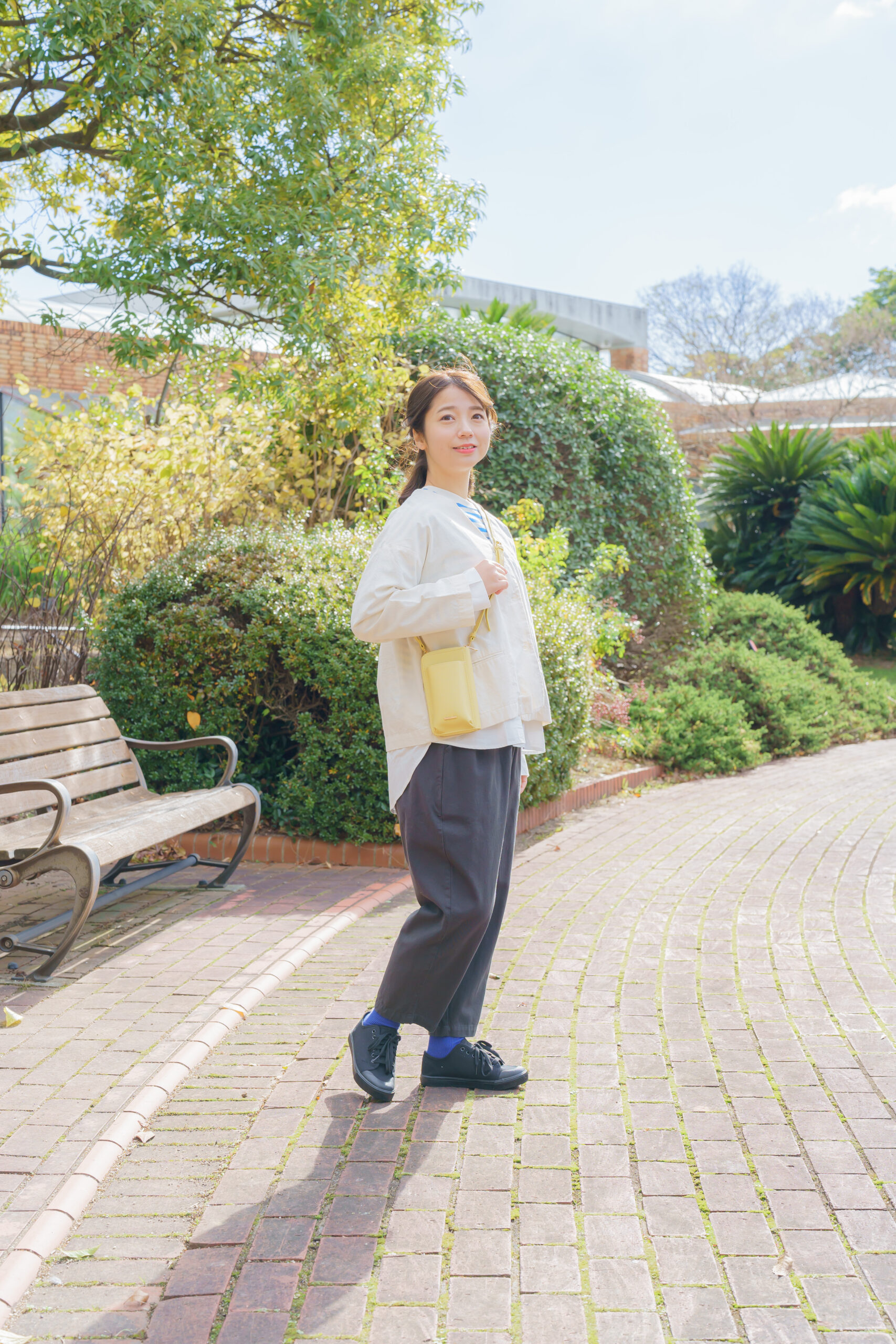 ベージュのブラウスにインナーには青ボーダーをきてグレーのパンツを履いて黄色のショルダーバックを身につけた女性