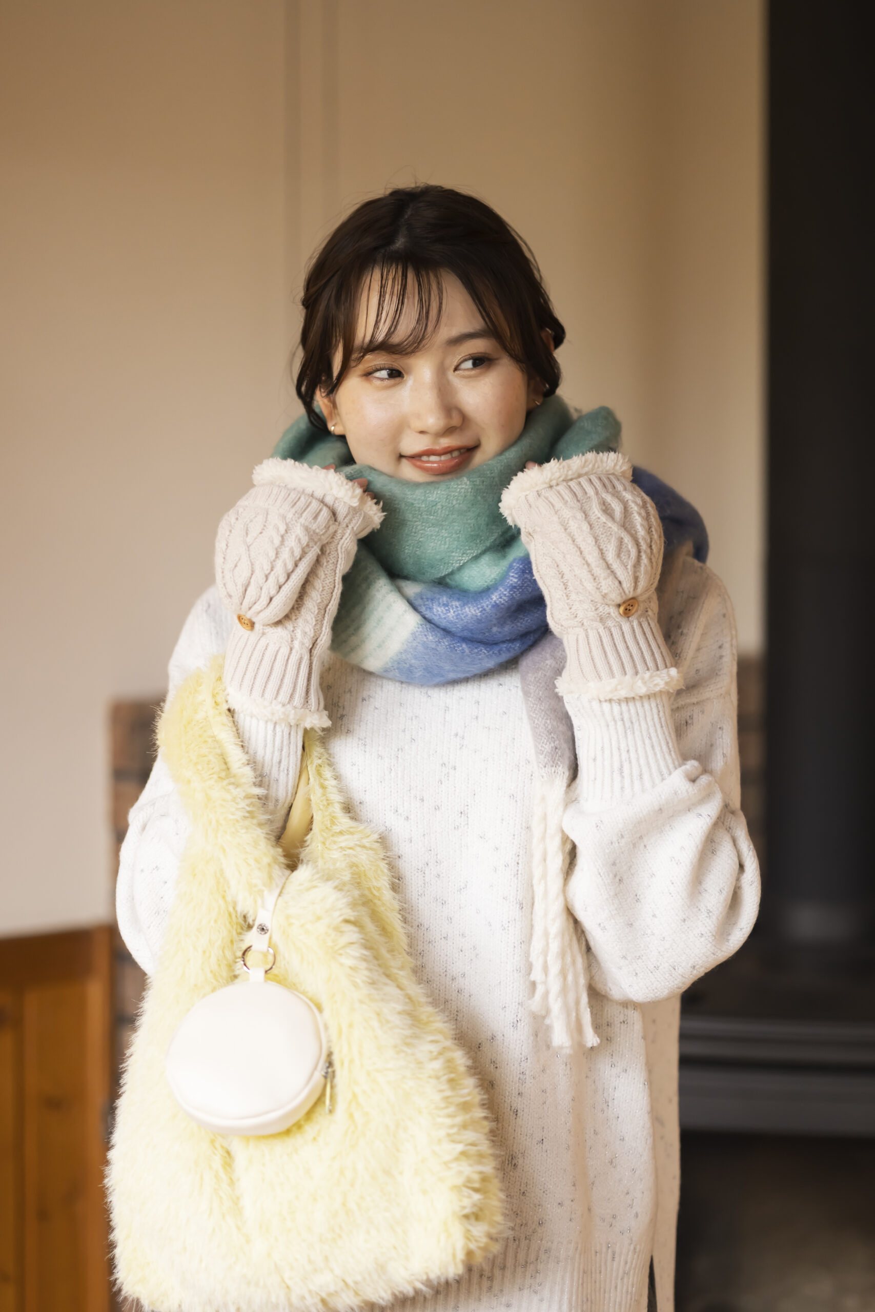 青みどりのチェック柄マフラーを巻き、アラン織柄の手袋をつけて黄色いシャギーバッグを持っている女性