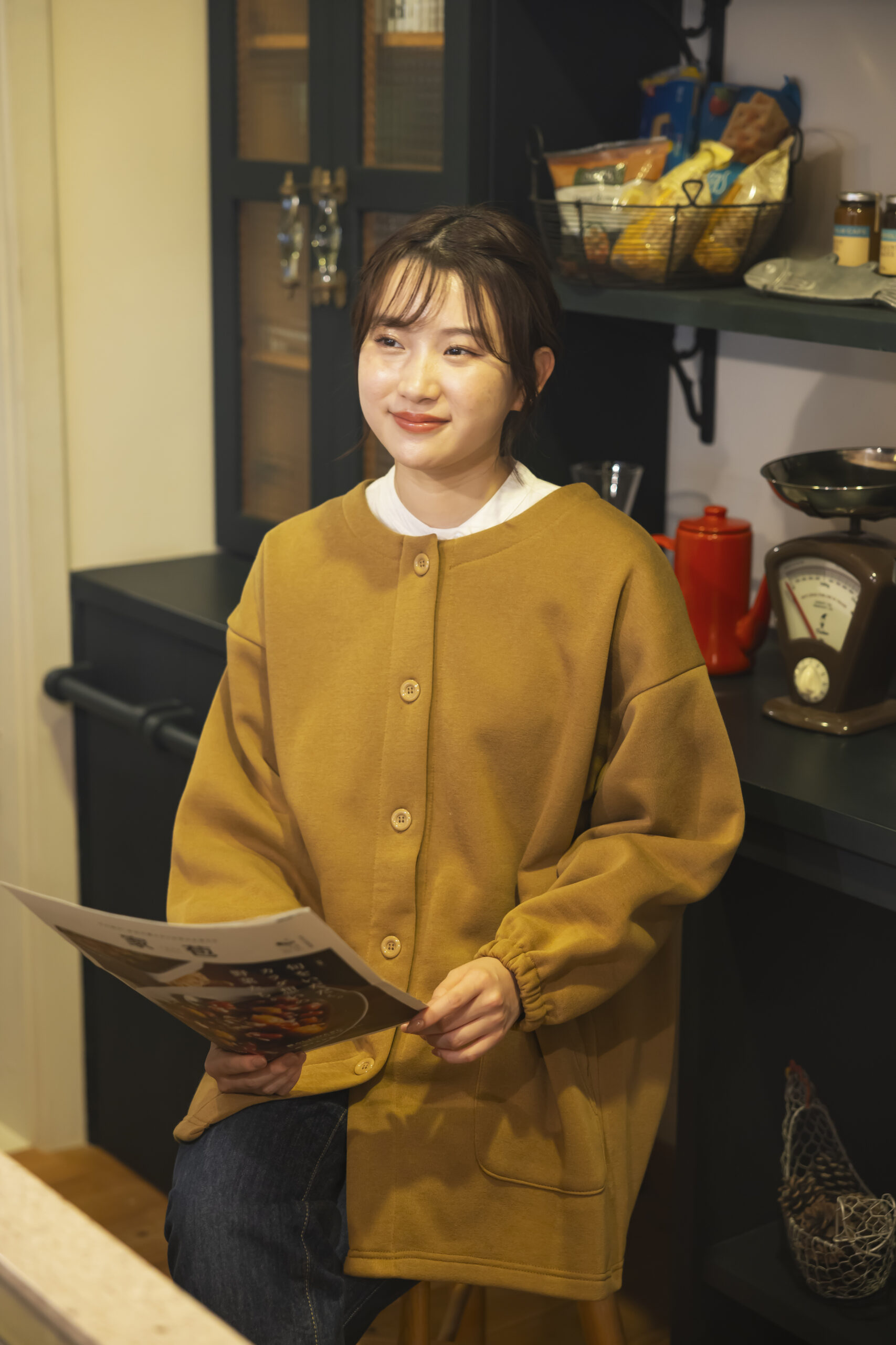 イエローオーカー色のカーディガンエプロンを着て今日の献立を考えている女性