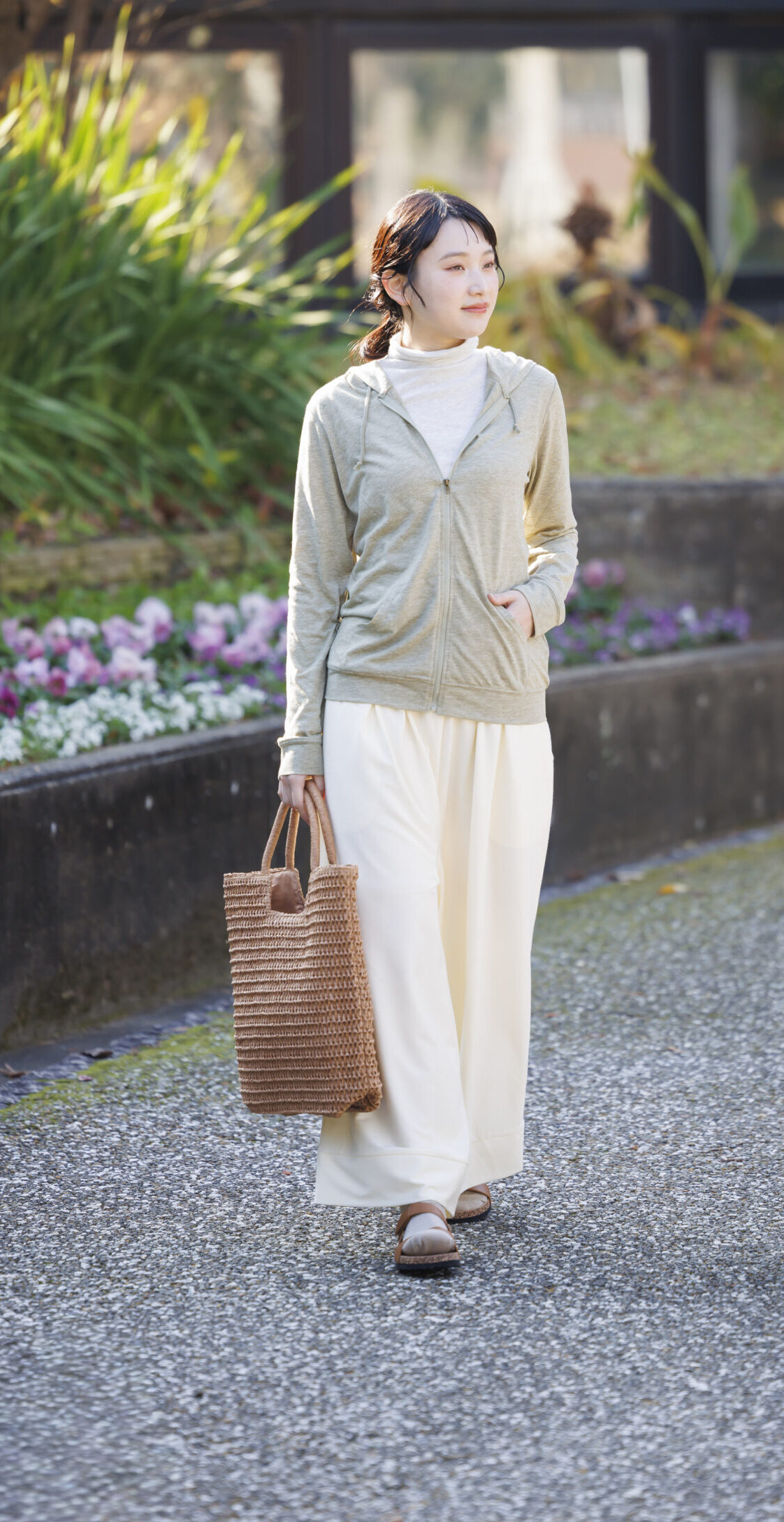 ボトルネックのインナーを着て緑のパーカーを羽織り白のワイドパンツを履いてバッグを持っている女性