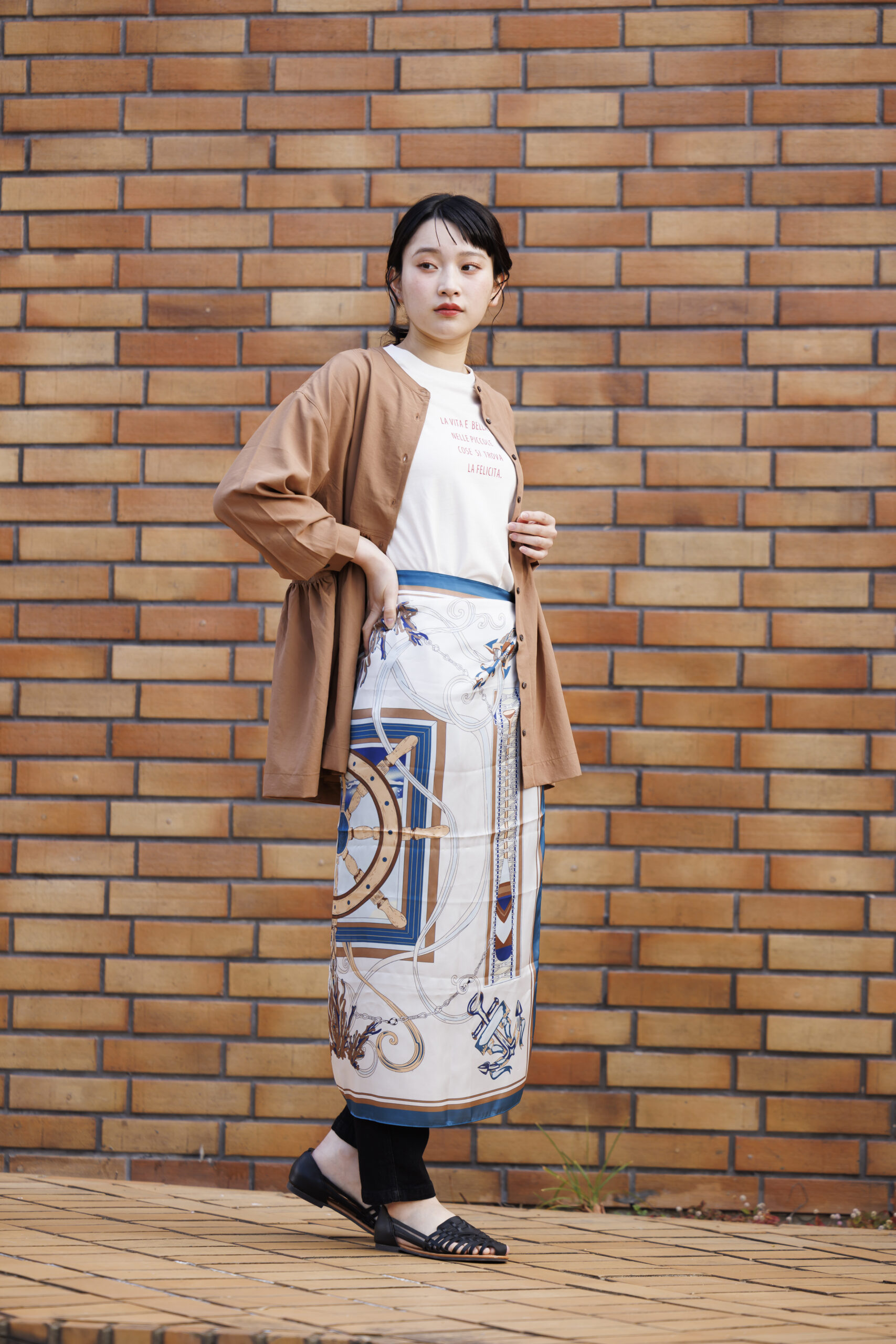 白のTシャツを着てブラウン系のブラウスを羽織ってスカーフを腰に巻いている女性