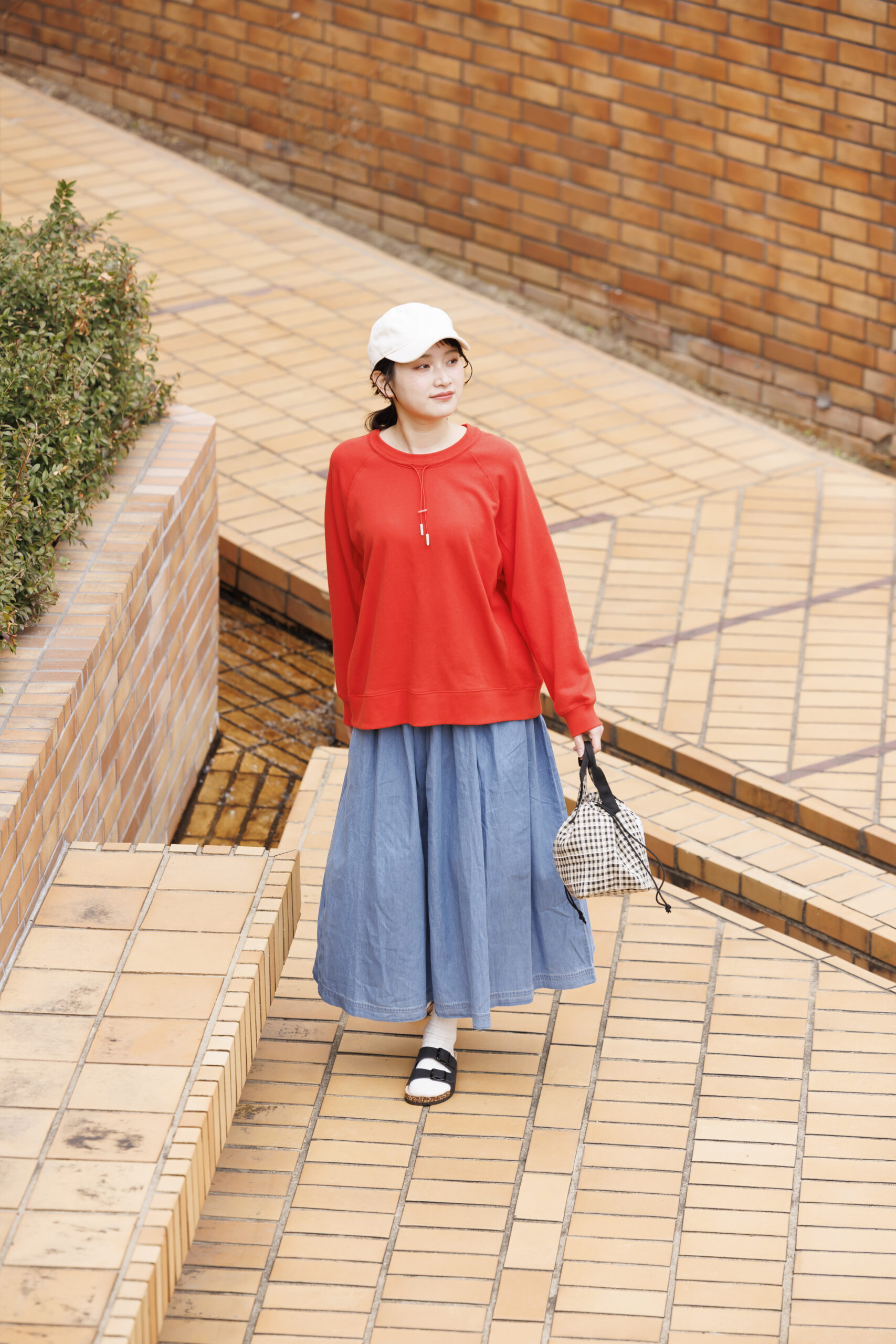 赤いカットソーを着てデニムスカートを履いて帽子を被ってバッグを持っている女性